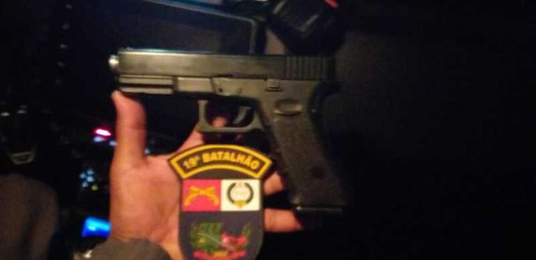 Policiais segurando simulacro de arma e moto apreendida após assalto em Tangará da Serra.